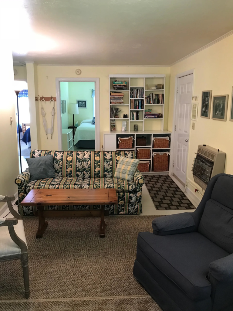 Cozy living room with a floral-patterned sofa, plaid cushions, a wooden coffee table, and a white cubby bookshelf against a light-yellow wall.
