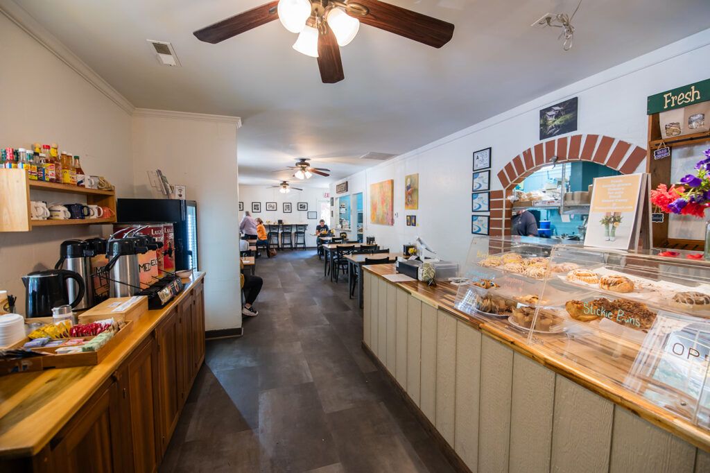 Café interior with a pastry counter on the right and a seating area down the hall, customers seated in the back room.