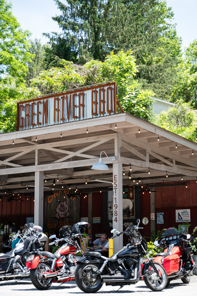 'green river bbq' sign on a rustic open-air eatery with string lights and motorcycles parked in front.