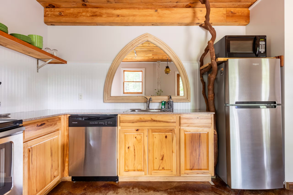 Kitchen with natural wood cabinets, stainless appliances, and a large arched mirror centered above the sink area.