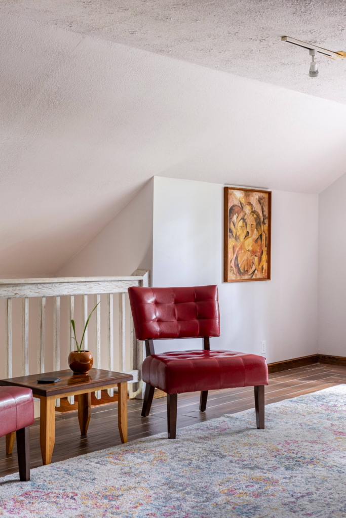 Red leather chair and matching ottoman in a bright living room with a small table, plant, and a colorful painting on the wall.