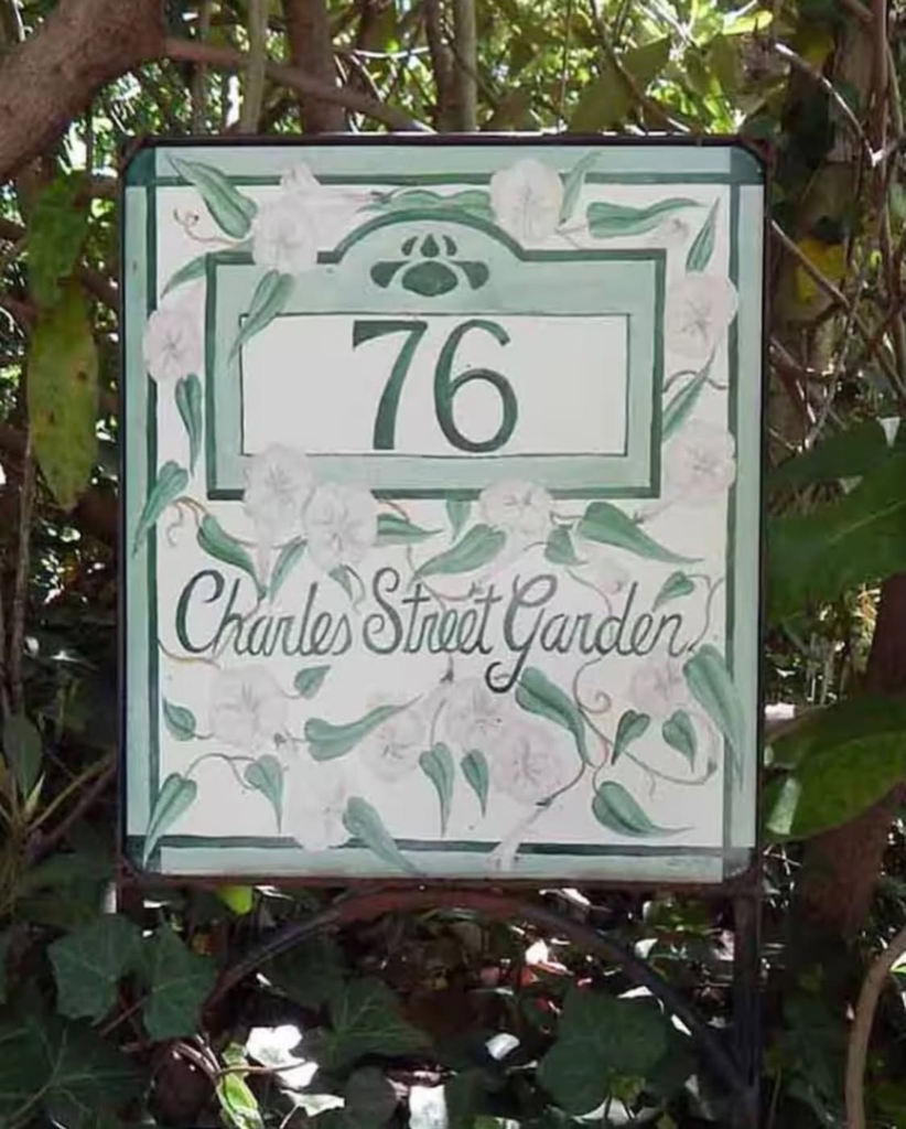 Address plaque for 76 charles street garden with a green floral border and white flowers.