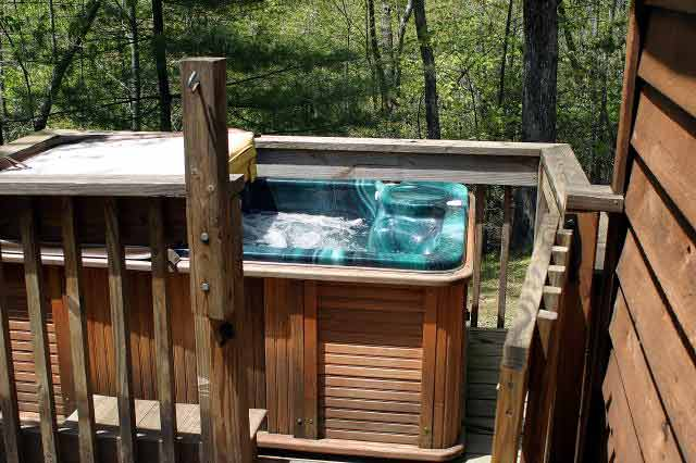Outdoor wooden deck with a hot tub, surrounded by trees in a backyard setting.