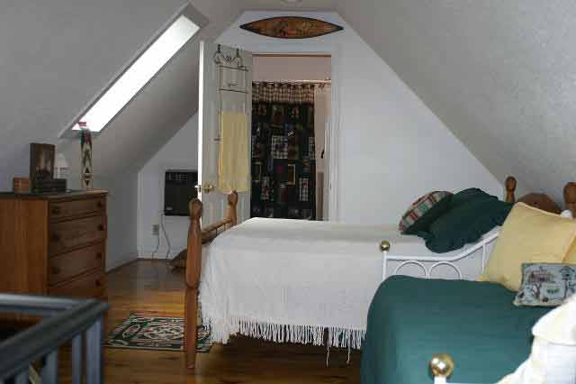 Attic bedroom with two wooden beds, white bedspreads, and a green couch facing the room; dresser on the left and a doorway to a closet in back.
