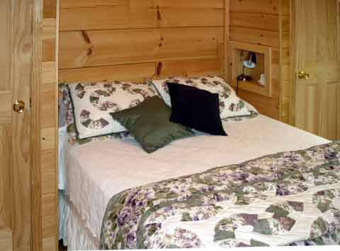 Cozy wooden bedroom with a quilted bed and multiple pillows.