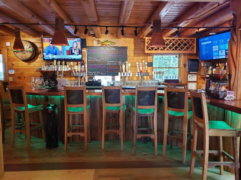 Rustic bar interior with wooden beams, chalkboard beer menus, and nine taps behind a wooden counter with high chairs.