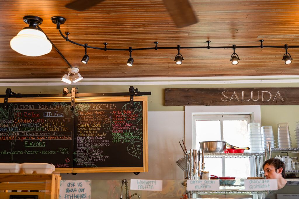 Cafe counter with chalkboard menus under a wooden ceiling and track lighting, partial bar area visible.