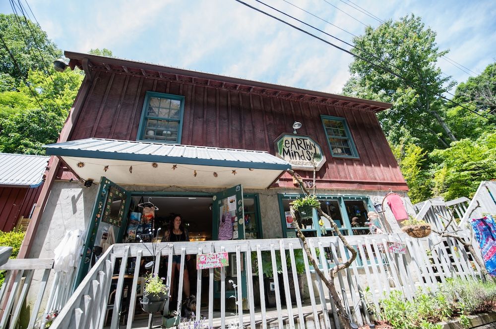 Colorful rustic two-story shop with a teal-trimmed door, open entrance, and a white picket fence; sign reads earthly minds gallery & gifts.
