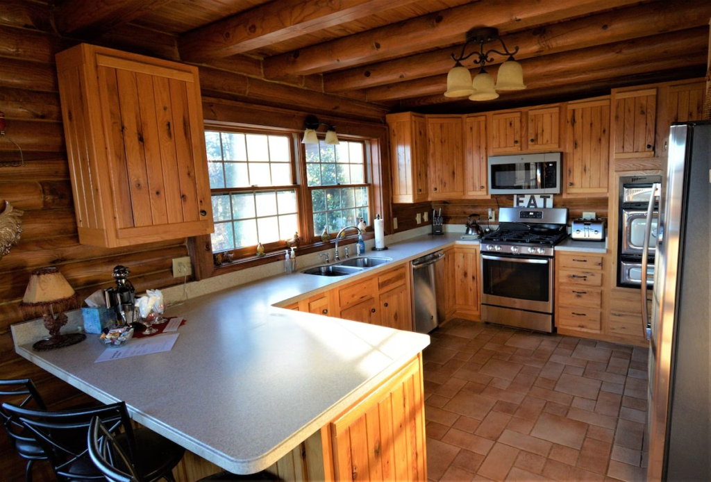 Rustic log-cabin kitchen with wooden cabinets, a light countertop island, and stainless steel appliances.