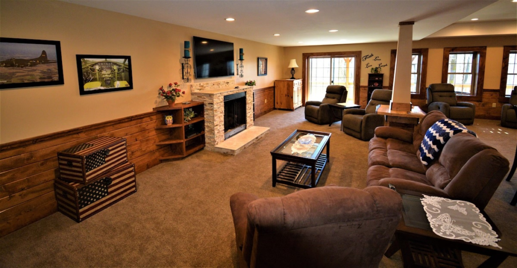Cozy living room with beige walls, a stone fireplace and a wall-mounted tv, surrounded by multiple brown recliners and a glass coffee table.