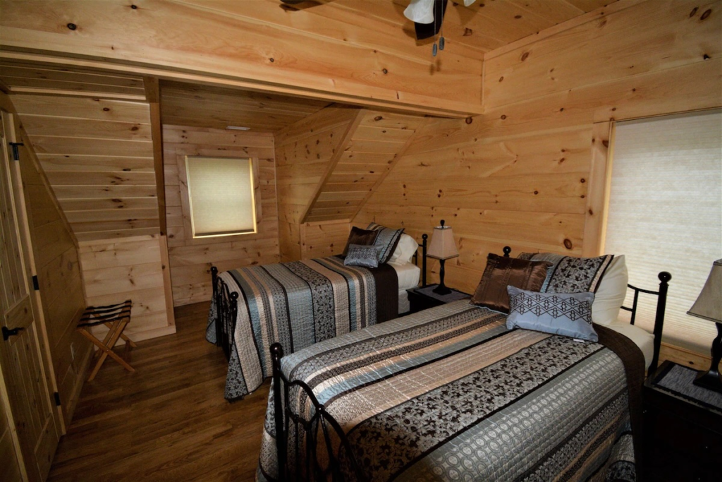 Cozy wooden bedroom with two queen/double beds, patterned quilts, and bedside lamps in a cabin interior