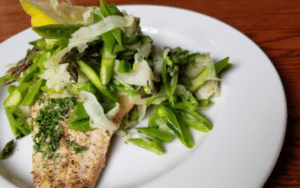 Pan-seared fish fillet with sautéed greens (asparagus or leeks) on a white plate, garnished with herbs.