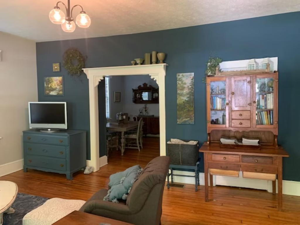 Living room with dark teal wall, a tv on a blue dresser, and a wooden hutch against the wall, hardwood floor.
