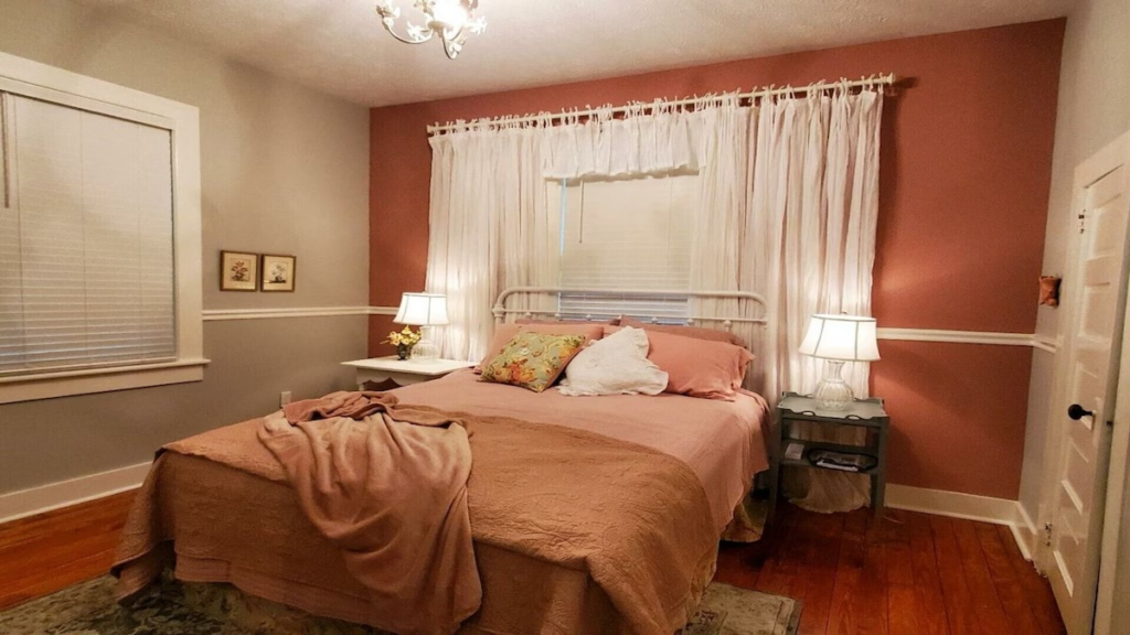 Cozy bedroom with pink bedspread, white metal bed frame, and matching nightstands with lamps on either side.