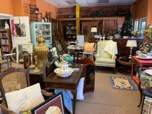 Interior of a antique shop with tables, chairs, cabinets, lamps, and decorative items on display.