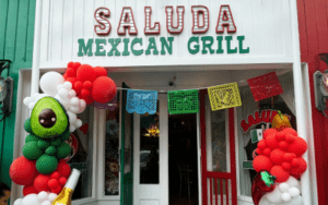 Entrance to Saluda Mexican Grill with a green and red facade, colorful bunting, and balloon columns at the entry.