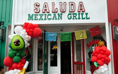 Entrance to Saluda Mexican Grill with a green and red facade, colorful bunting, and balloon columns at the entry.