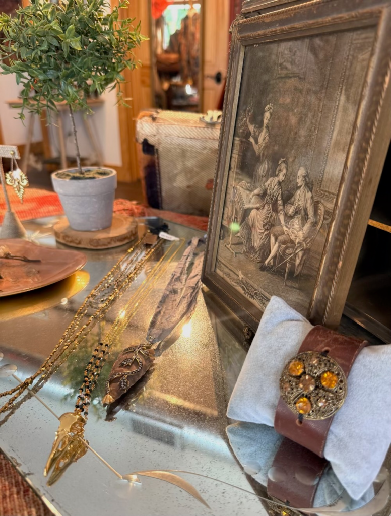 Display table with gold jewelry and a framed vintage print in a cozy boutique setting.
